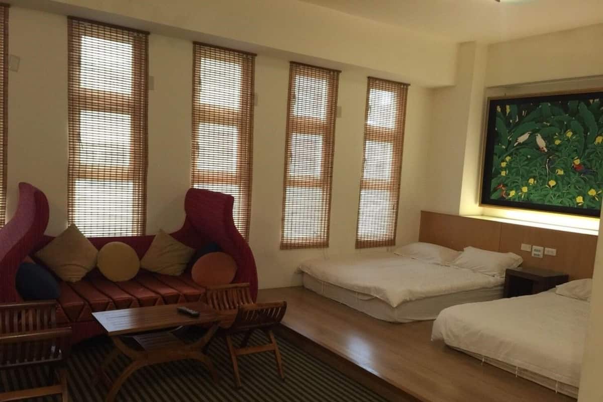 A hotel room with a sofa, two single beds, a small table, and a painting on the wall.