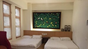 A hotel room with two beds, a large painting above the beds, and a small table with a chair. - U-Lu B&B (Hualien City)