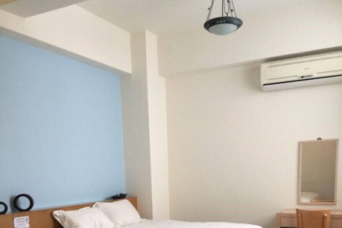 A hotel room with two beds, a desk, and an air conditioning unit.