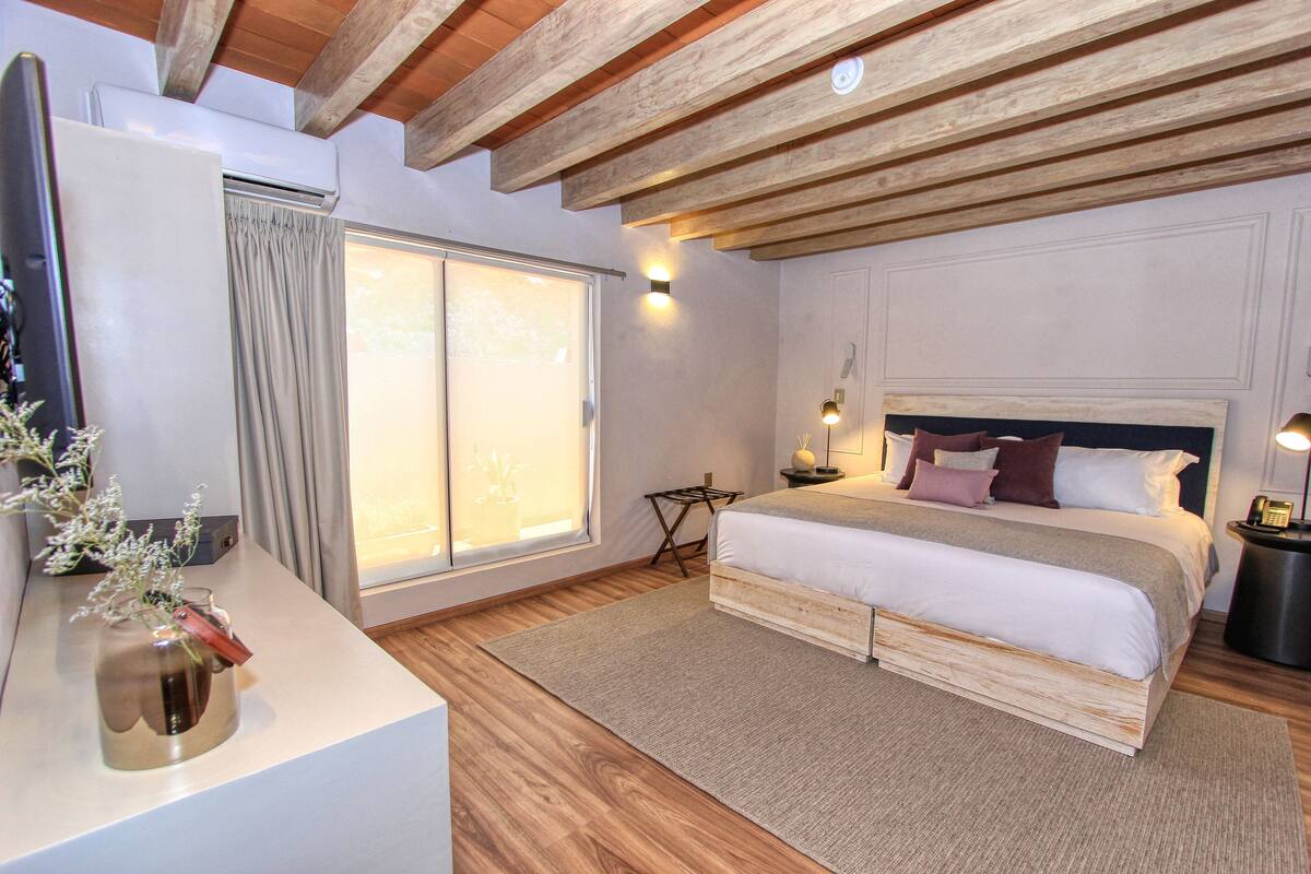 Ein Schlafzimmer mit einem Bett, Nachttischen, einem Fenster mit Vorhängen und einer Wand-Klimaanlage.
