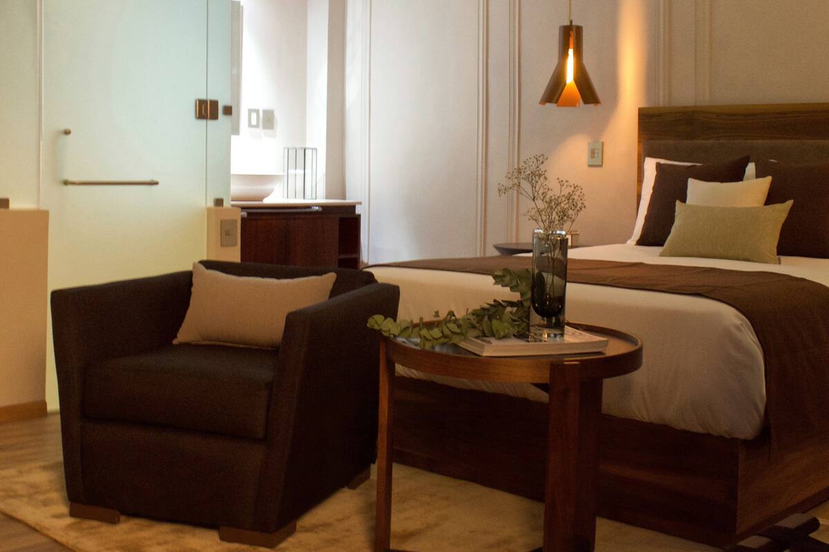 Ein Hotelzimmer mit einem Bett, zwei Sesseln, einem kleinen Tisch mit einer Vase und einer Pendelleuchte.