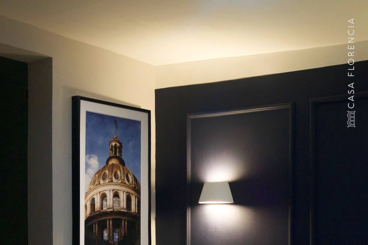 Ein Hotelzimmer mit einem großen Bett, einem gerahmten Bild eines Gebäudes an der Wand, einer Nachttischlampe und einem Nachttisch.