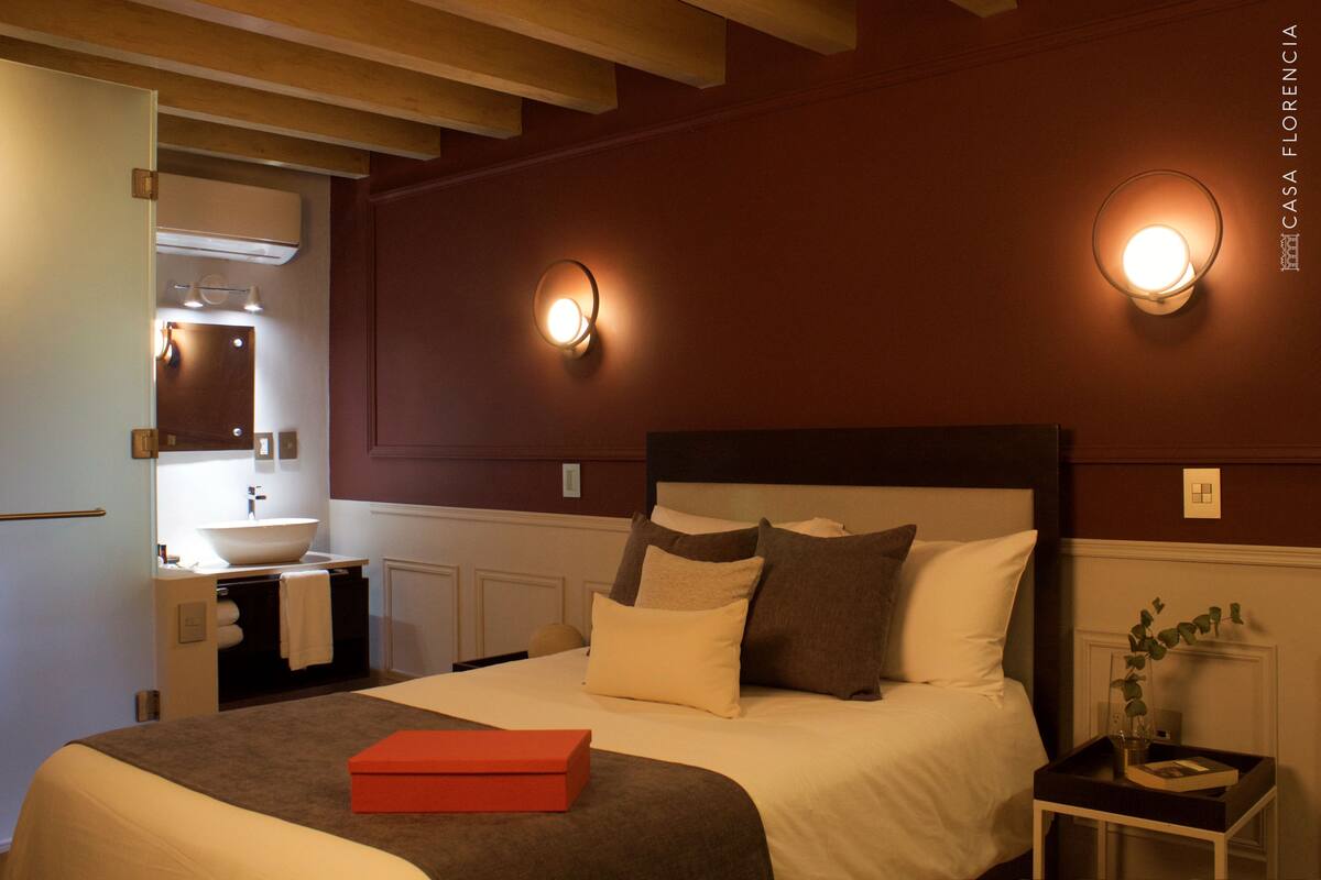 Ein Hotelzimmer mit Bett, Nachttisch und einem Badezimmer mit Waschbecken und Spiegel.