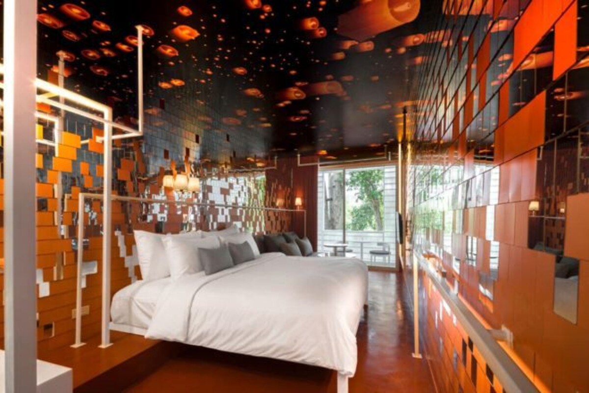 A modern hotel room with a large bed, a unique ceiling design, and large windows.