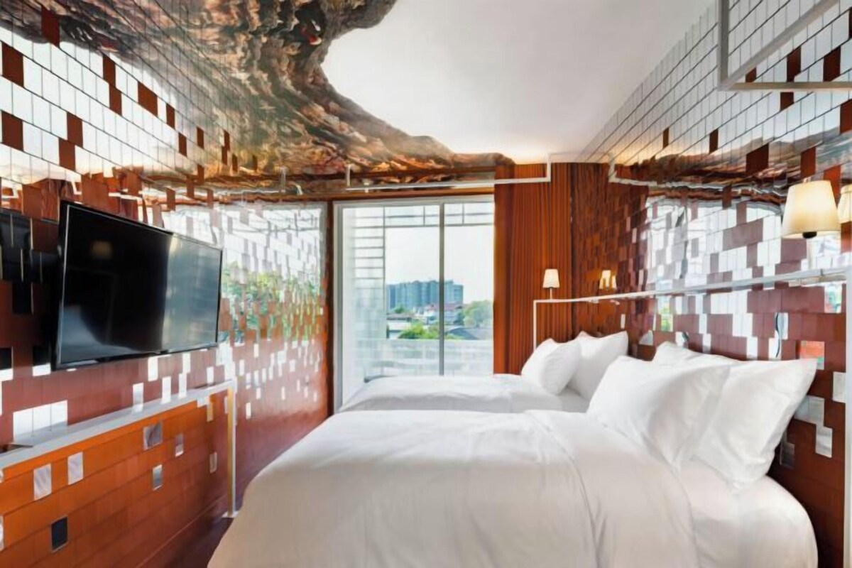 A modern hotel room with a large bed, a flat-screen TV, and a city view through large windows.