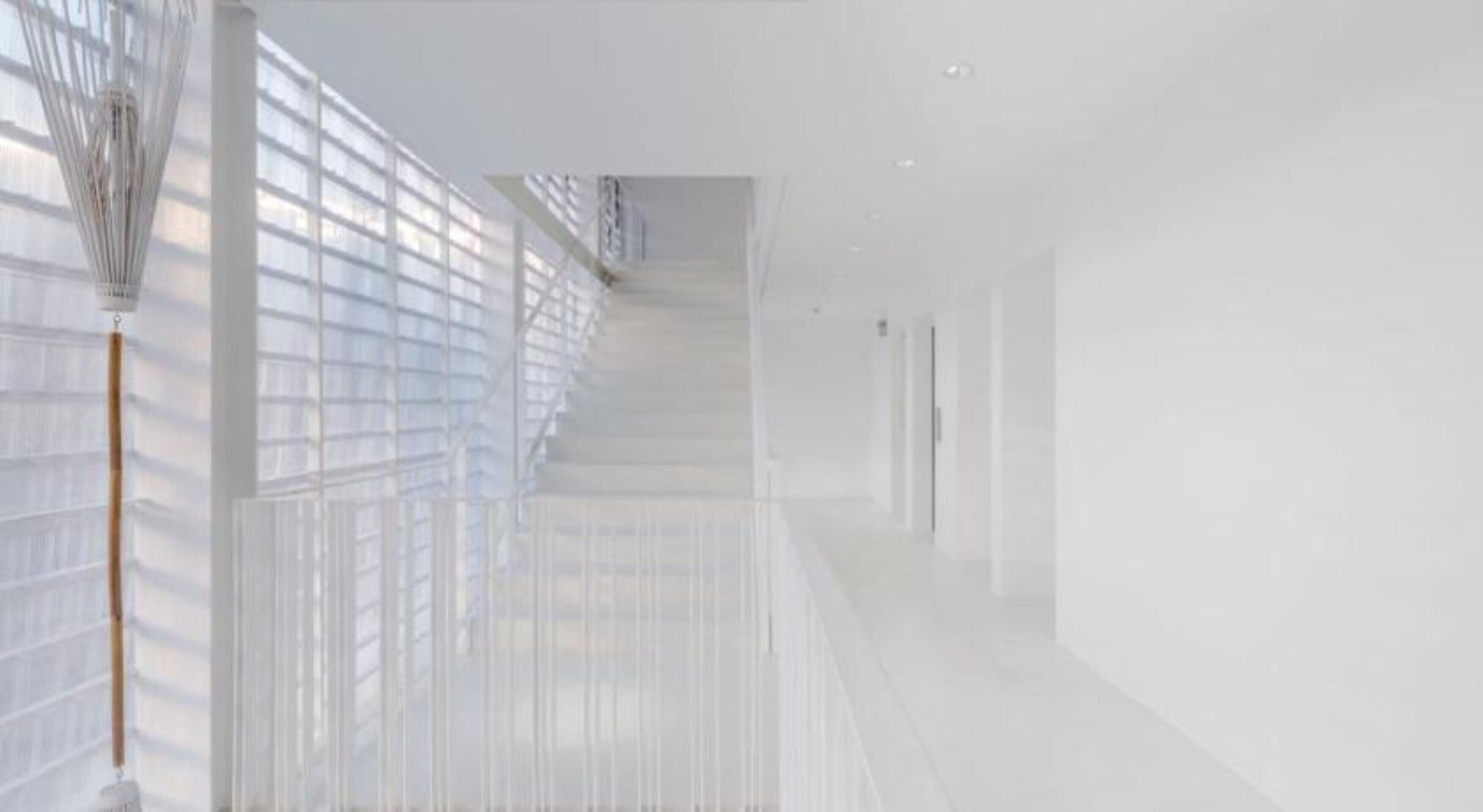 A bright, modern hallway with large windows, a wooden floor, and a staircase leading to an upper level.