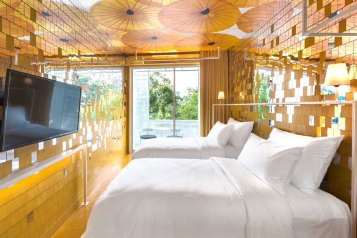 A hotel room with a large bed, a TV mounted on the wall, and a view of greenery outside.