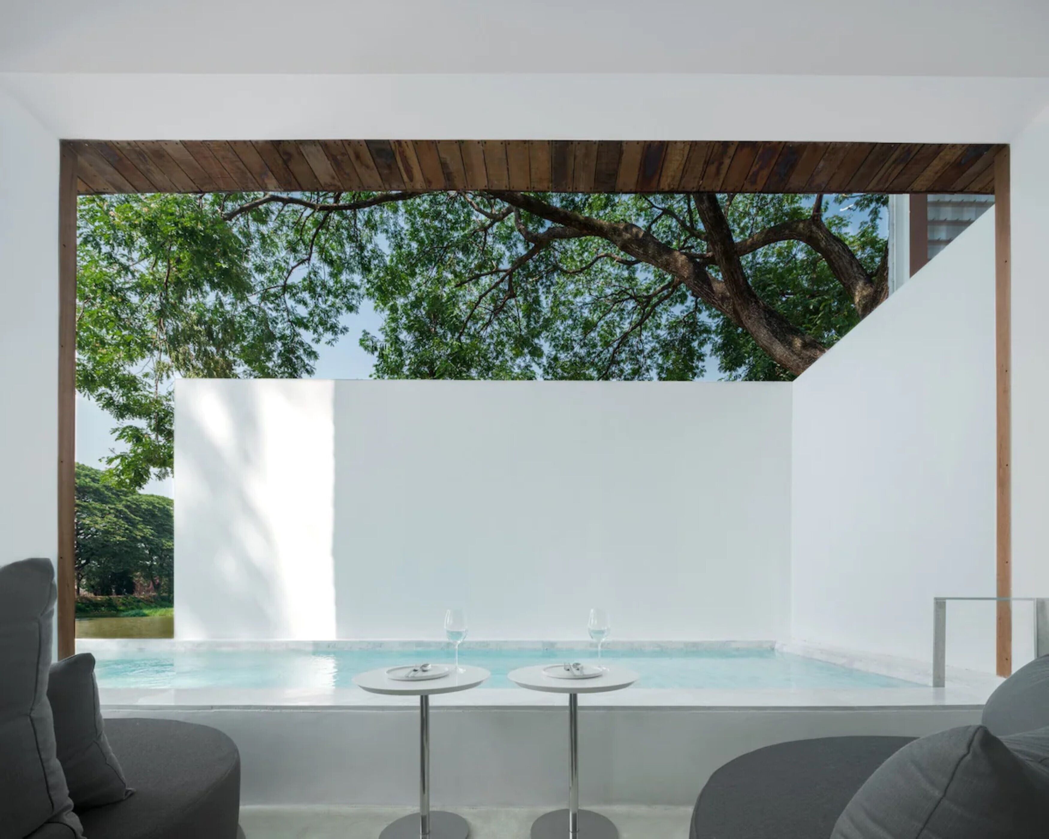 A modern outdoor seating area with two tables and chairs, overlooking a clear pool and lush greenery.