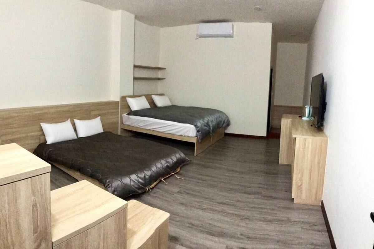 A compact hotel room with two single beds, a wooden nightstand, a small desk, and a television.