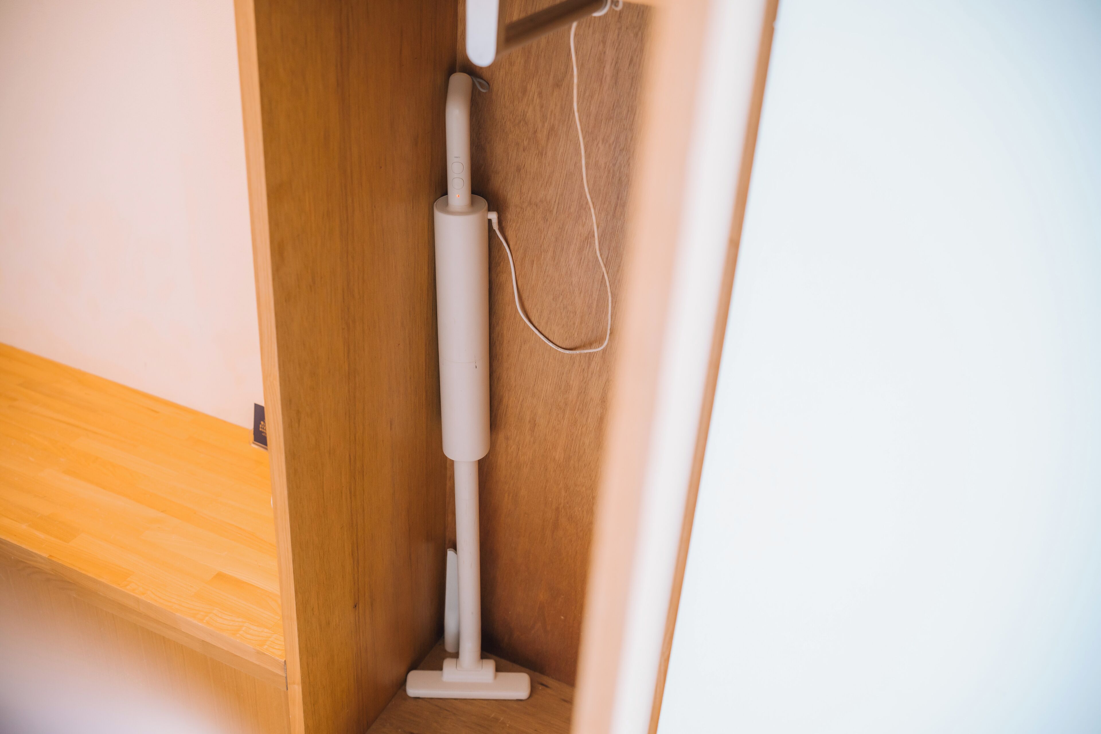 A corner of a room with a wooden floor, a white object that appears to be a vacuum cleaner, and a cable hanging from it.