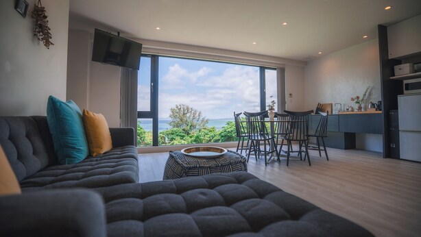 A modern living room with a sofa, ottoman, and dining area with chairs. - BLUE STEAK WONDER SENAHA (Yomitan)