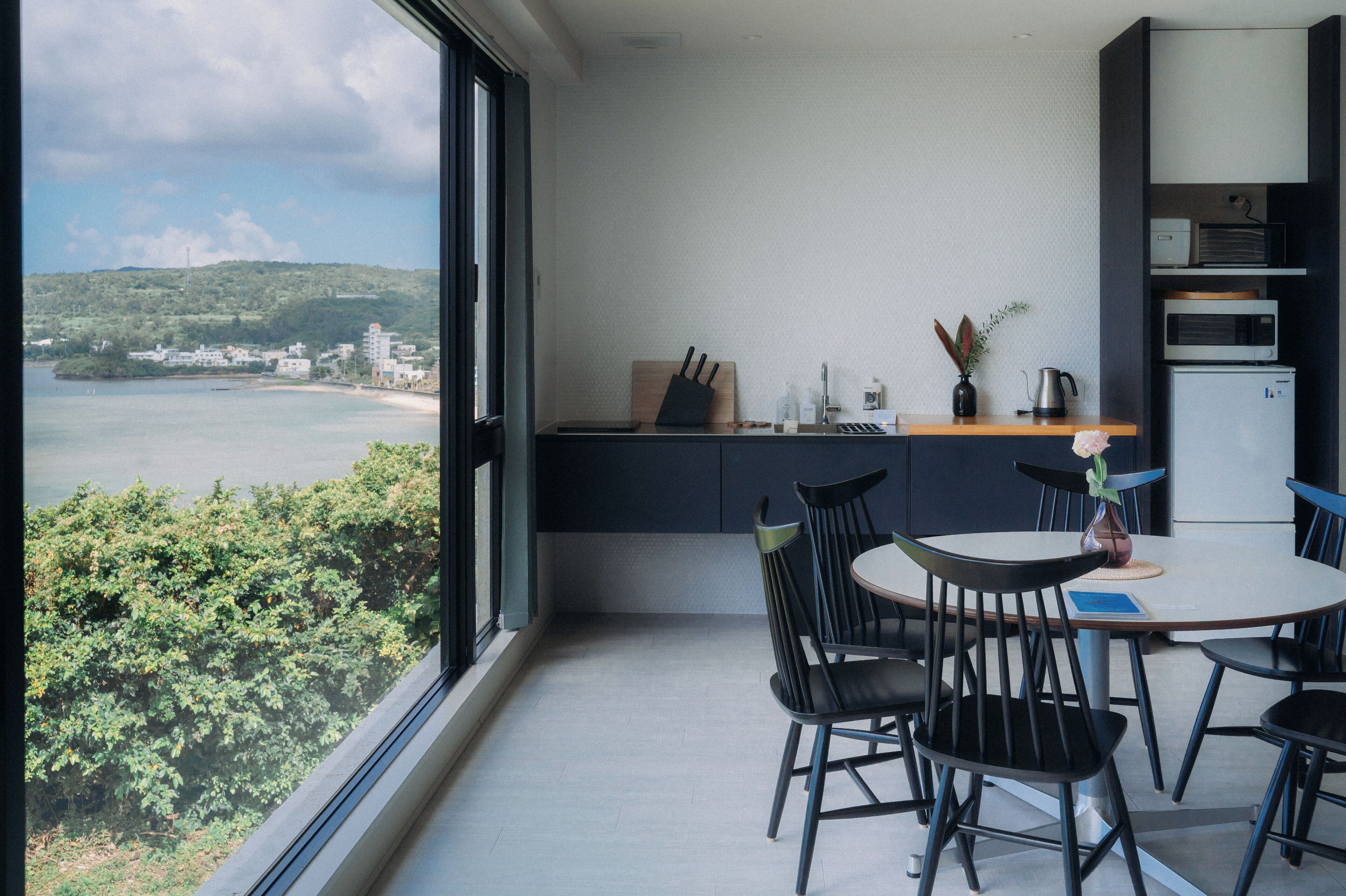 A modern dining area with a view of a coastal landscape, a kitchen area with appliances, and a dining table with chairs.