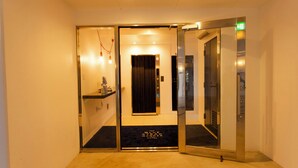 An elevator with a glass door and a black mat with hotel name. - BLUE STEAK WONDER SENAHA (Yomitan)