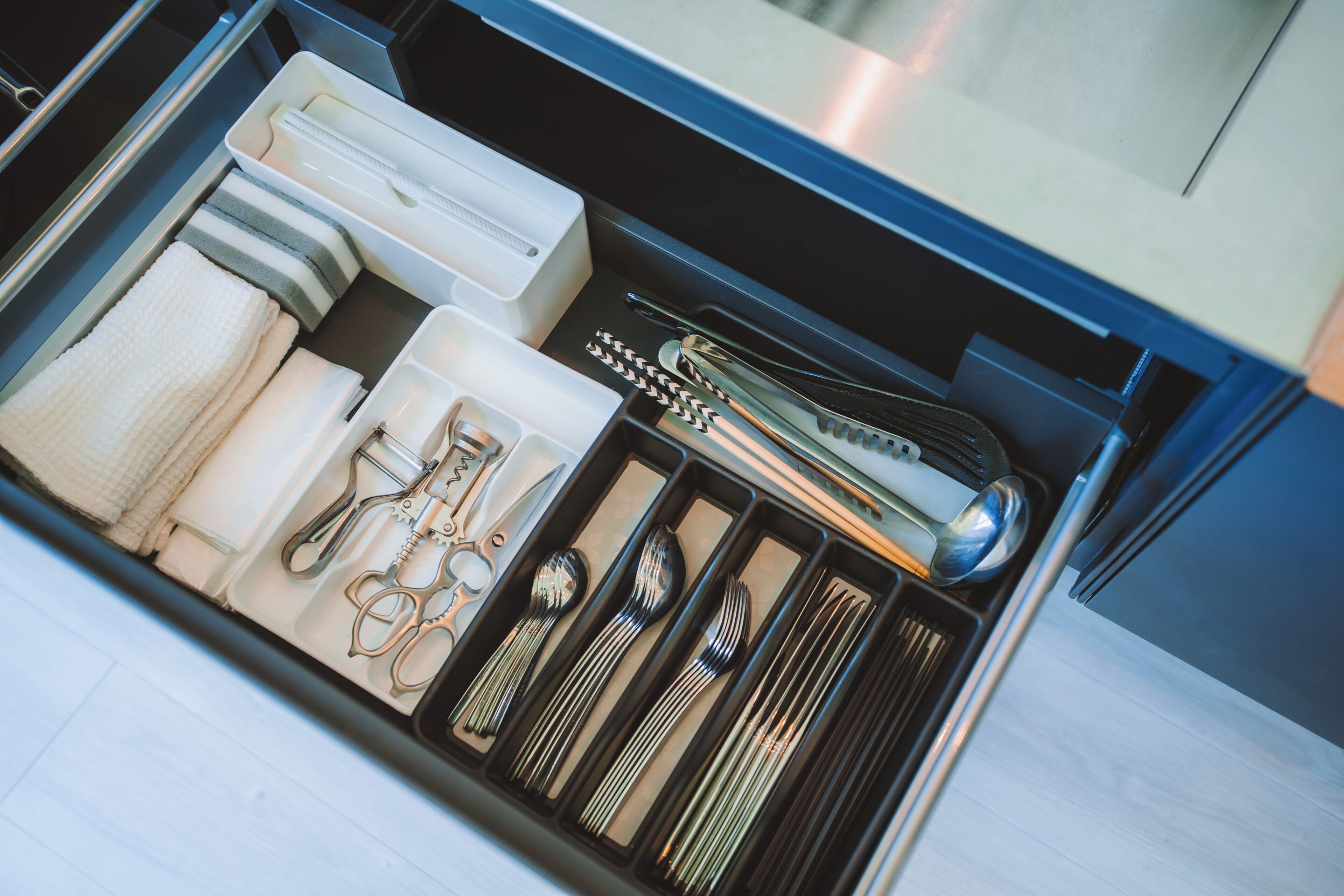 A drawer with neatly organized kitchen utensils, including spoons, forks, and a whisk.