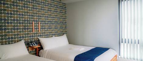 A hotel room with two beds, a patterned wall, a nightstand, and a window with blinds.