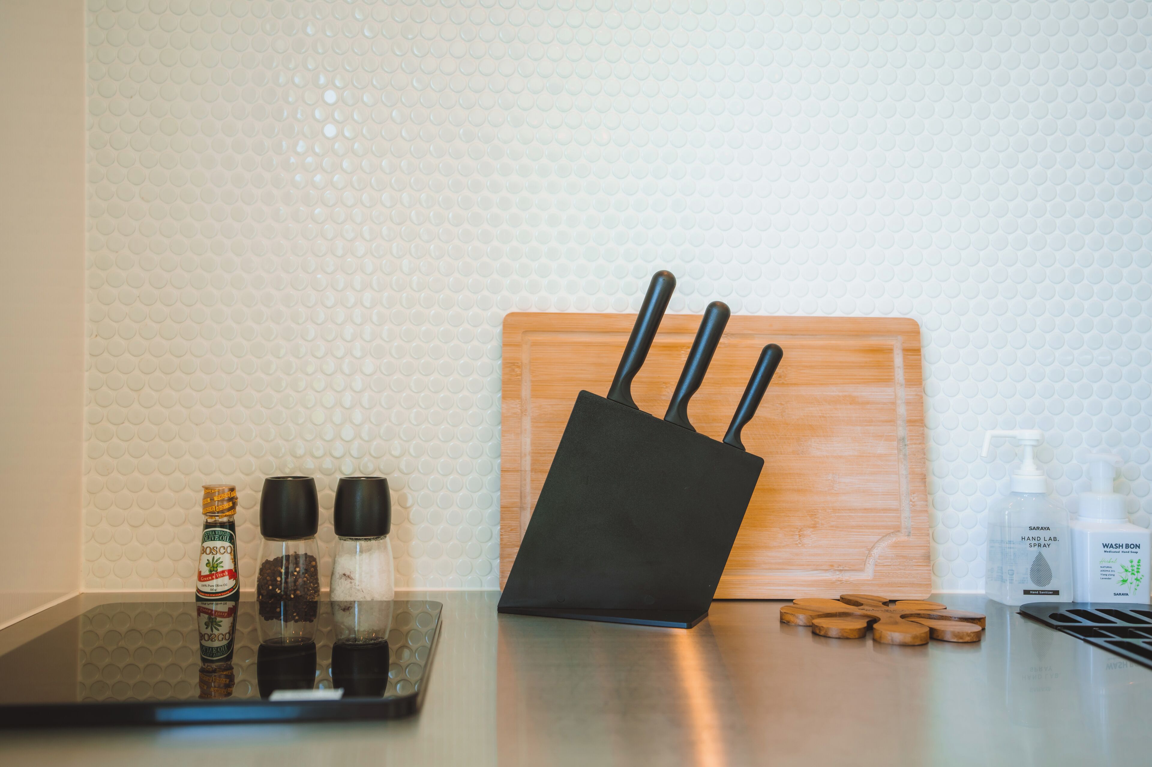 A kitchen counter with a black router, wooden cutting board, pepper and salt shakers, a bottle of hand soap, and a hand sanitizer dispenser.