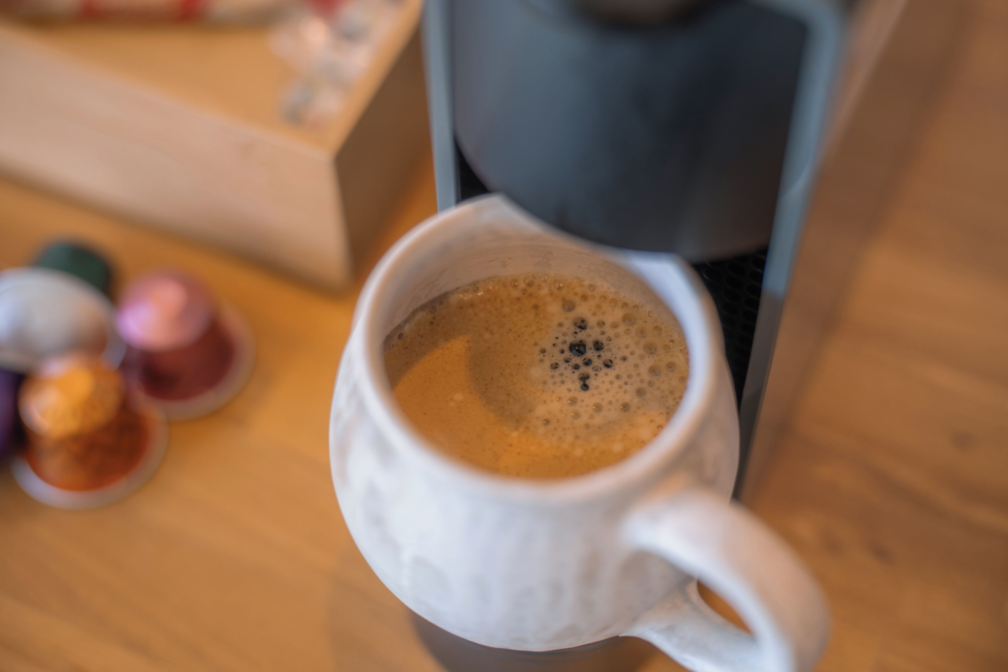 A white ceramic mug with a handle, filled with a frothy beverage, likely coffee, on a wooden surface.