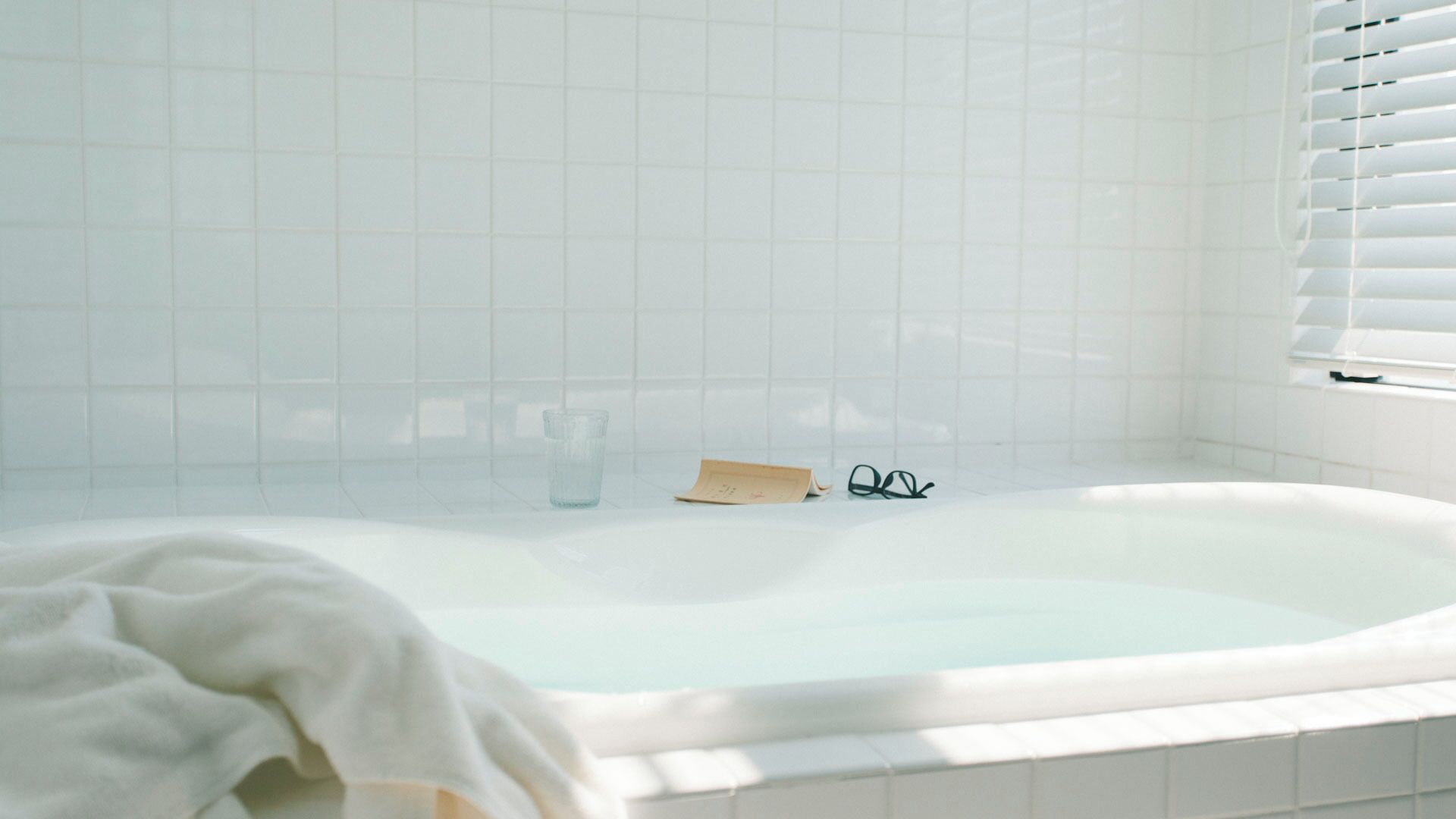 A white bathtub with a glass of water, a pair of glasses, and a towel.
