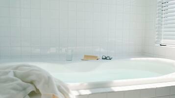 A white bathtub with a glass of water, a pair of glasses, and a towel.
