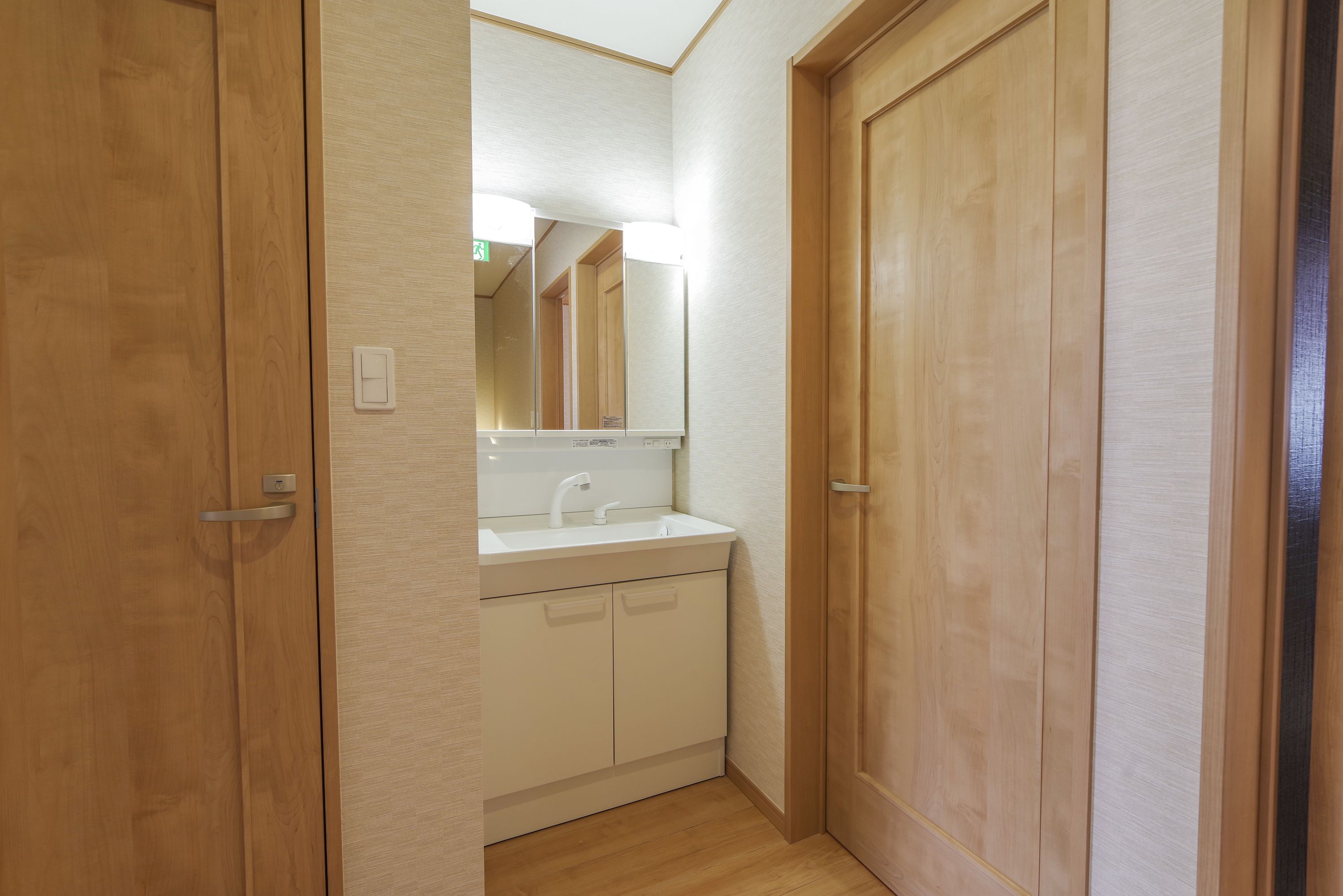 A narrow hallway with wooden doors and a white sink with a mirror above it.