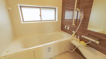 A bathroom with a bathtub, a window, a shower, and a vanity with toiletries.