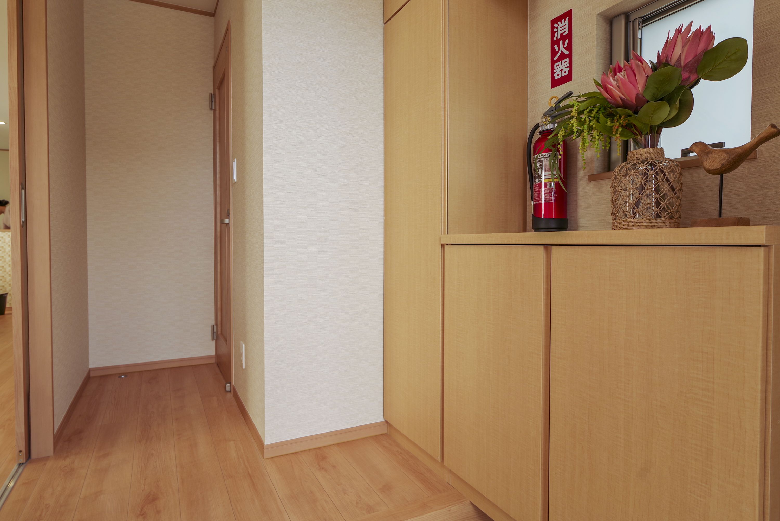 Ein Flur mit Holzboden und einem Holzschrank, der eine Blumenvase und einen Feuerlöscher enthält.