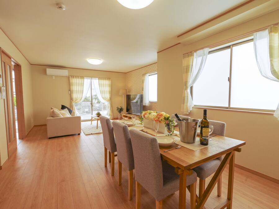 A modern living room with a dining area, wooden flooring, and large windows with curtains.