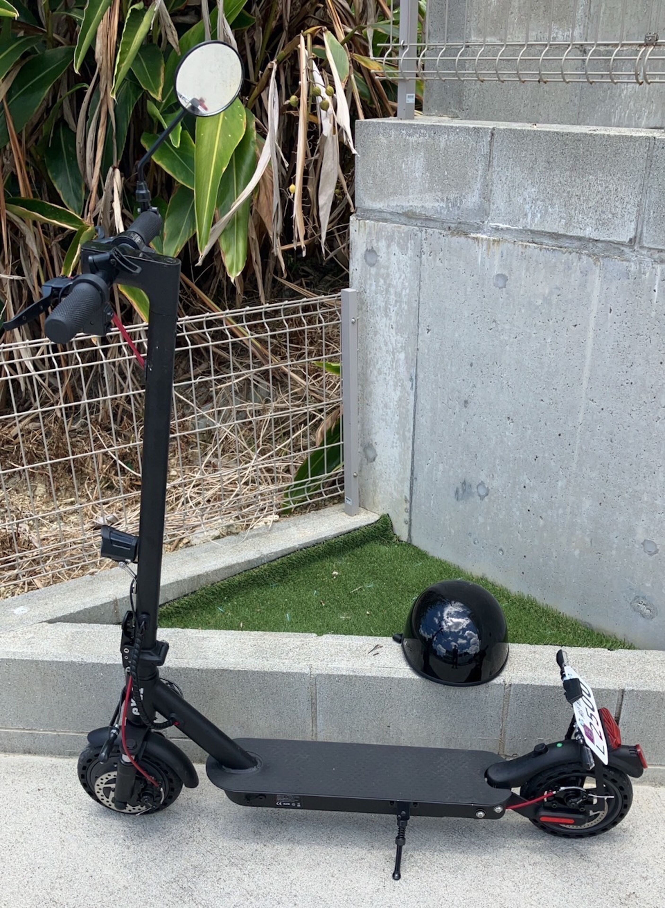 A black electric scooter parked on a concrete surface with a helmet beside it.