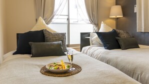 A hotel room with two beds, a dining table with a salad and a glass of wine, and a lamp on the nightstand. - Hyakuna Terrace (Nanjo)