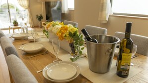 A dining table set with plates, cutlery, a wine bottle, a glass, and a flower arrangement. - Hyakuna Terrace (Nanjo)