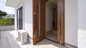 A modern building entrance with a wooden door and a white air conditioning unit outside. - Hyakuna Terrace (Nanjo)