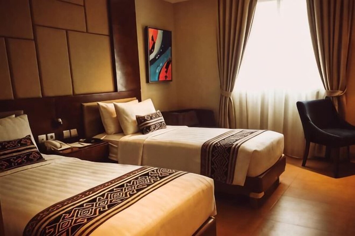 A hotel room with two beds, a desk, a chair, and a painting on the wall.
