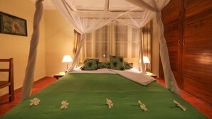 A room with a bed, two bedside lamps, a wooden wardrobe, and a window with curtains.