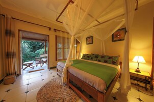 Quarto com cama, mesa de cabeceira com abajur, janela com cortinas e vista para o exterior.
