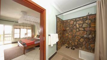 A bedroom with a bed, a bathroom with a stone wall, and a shower.