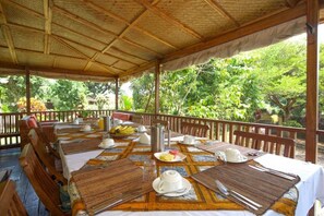 An outdoor dining area with tables set for breakfast, surrounded by lush greenery.