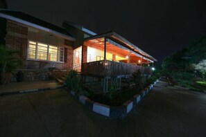 A two-story building with a balcony and a covered outdoor area, surrounded by a landscaped garden.