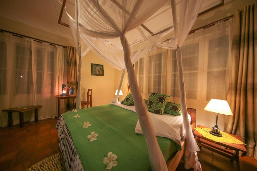 Un dormitorio con una cama con dosel, una mesita de noche con lámpara y un banco.