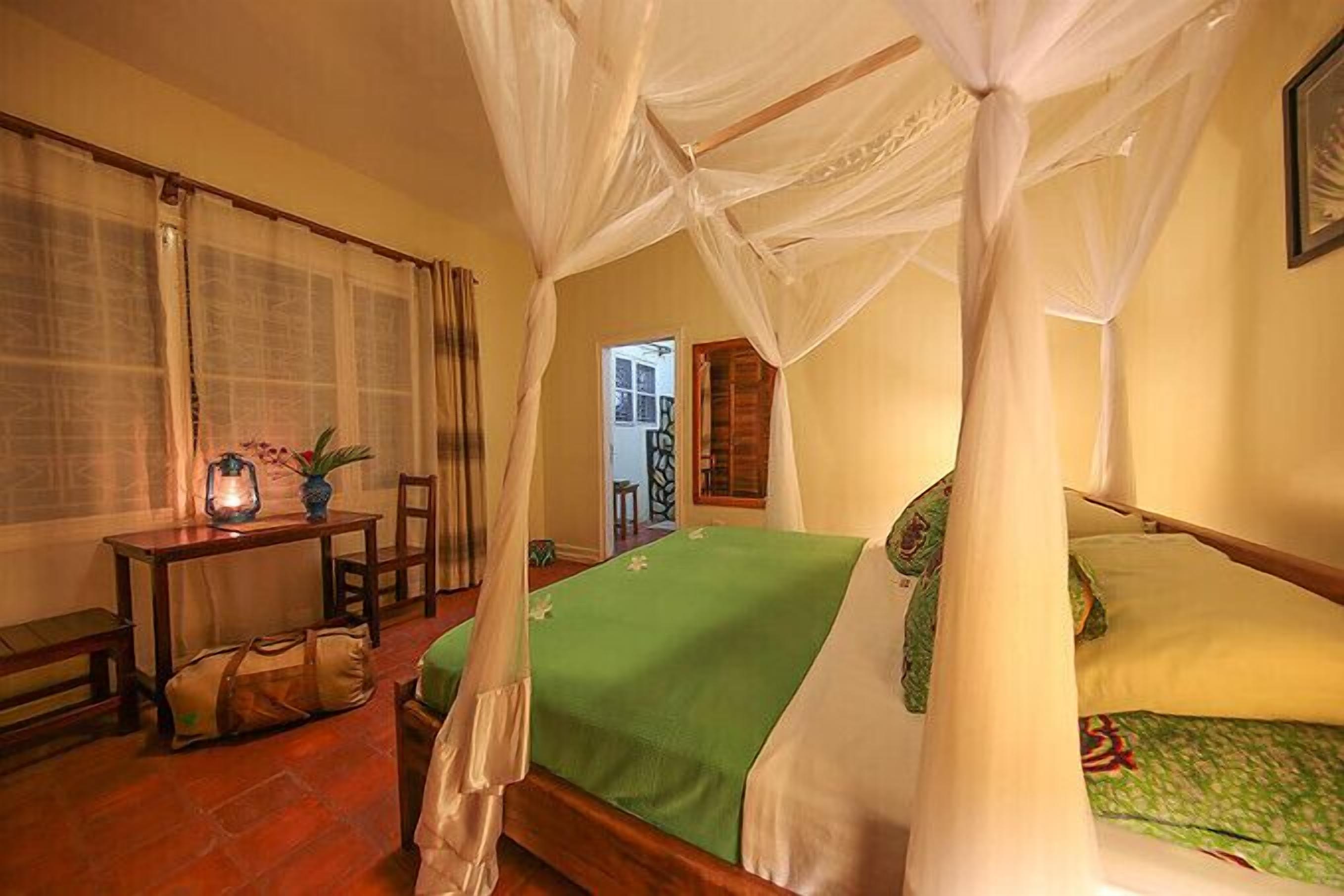 A room with a bed, a table with a lantern, and a chair.