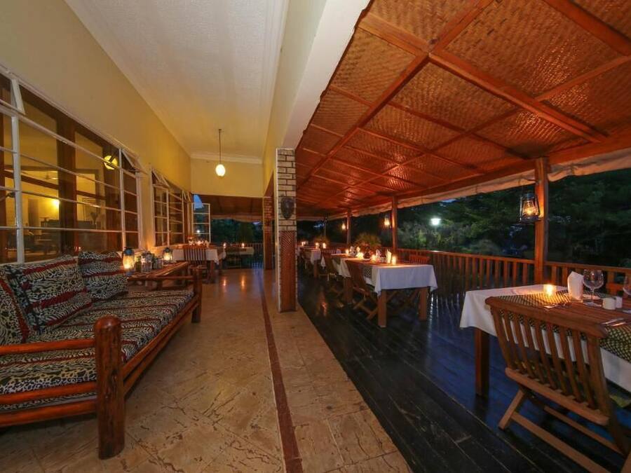 An outdoor dining area with wooden furniture and tables, a covered section with a woven roof, and a view of the outdoors.