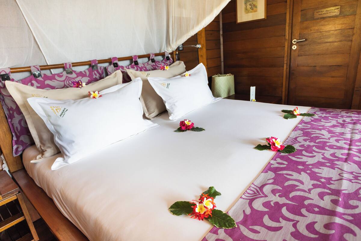 A neatly made bed with a canopy, pillows, and decorative flowers.
