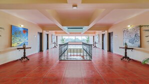 Un corredor espacioso con una escalera central, flanqueado por obras de arte y plantas en macetas.