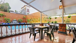 Un patio al aire libre con mesas y sillas, una piscina y plantas en macetas.
