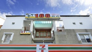 Un edificio con una tienda 7-Eleven en la planta baja, un balcón con barandilla y un letrero con el número 166.