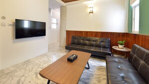 Una sala moderna con un televisor de pantalla plana, una mesa de centro de madera, un sofá de cuero y una pequeña mesa redonda con una planta.