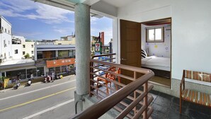 Una habitación de hotel con balcón, vista a la calle y una tienda 7-Eleven al fondo.
