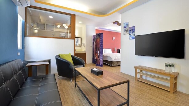 Una habitación de hotel moderna con sofá, una mesa de centro de madera, un televisor y una mesita con una botella.
