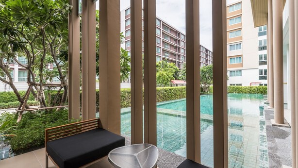 A modern hotel room with a view of an infinity pool, a wooden bench, and a glass table.