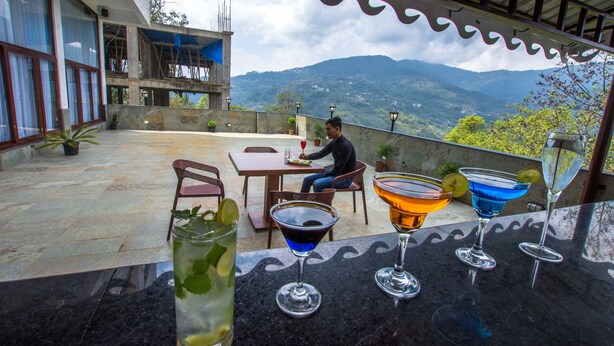 A terrace with a table and chairs, a bar area with various drinks, and a view of mountains. - Mount Himalayan Hotel (Gangtok)