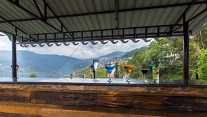 A wooden bar with a view of mountains and a village. - Mount Himalayan Hotel (Gangtok)